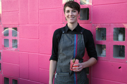 Woman wearing Savilino bib apron with colorful piping against a pink wall