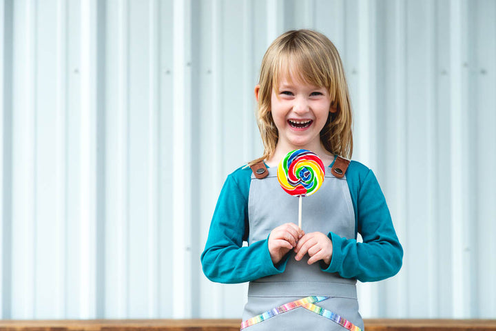 Young girl wearing kids' grey Savilino apron with rainbow piping.
