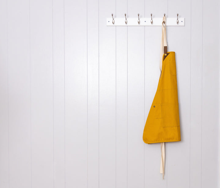 Savilino mustard color bib apron hanging on white wall