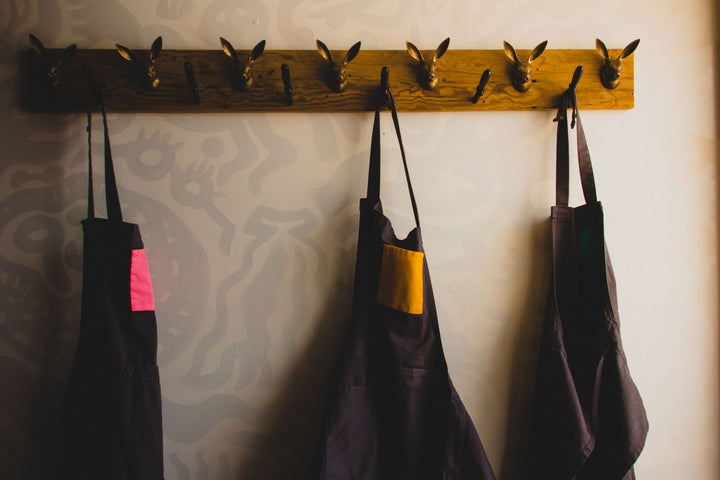 Several Savilino bib aprons hanging in a kitchen entry. 