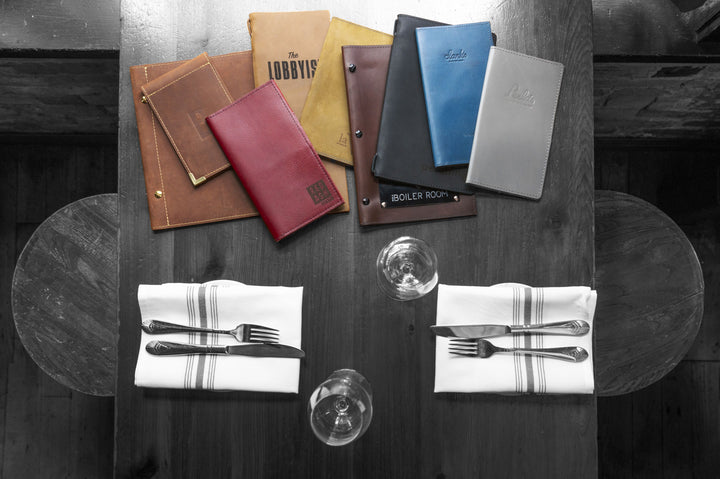 Grouping of Savilino leather menus in different colors laid out on a restaurant table.